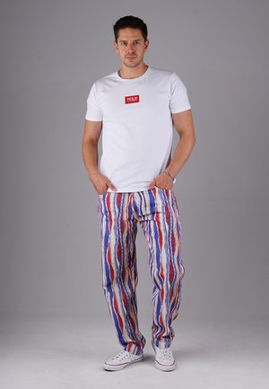 White short-sleeve t-shirt with a red logo, paired with colorful striped pants in blue, red, and gold tones. White canvas sneakers.