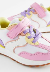 Baskets colorées avec une base textile blanche, présentant des accents roses, lavande et jaunes. Conçues avec des lacets et une bande velcro.