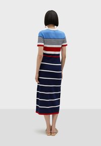 Koftklänningen har horisontella ränder i blått, rött, vitt och marinblått. Den har midilängd, korta ärmar och enfärgade detaljer vid fållen.