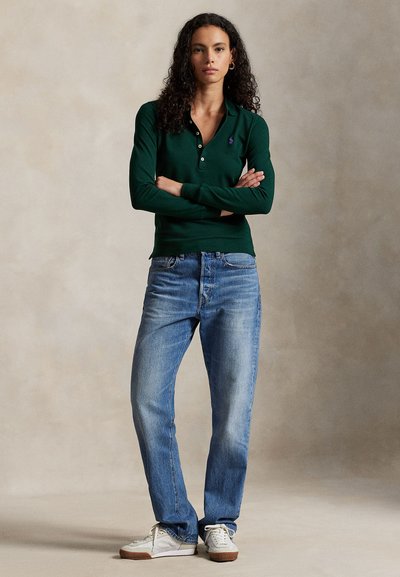 Ciemnozielona koszulka polo z długim rękawem i plisą na trzy guziki, zestawiona z jasnoniebieskimi, prostymi jeansami i białymi trampkami.