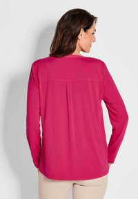 Langärmliges Shirt in lebhaftem Pink, mit Rundhalsausschnitt und einem dezenten Rückenfalten für Bewegungsfreiheit und Passform.