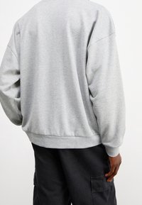 Grå sweatshirt med lös passform, med en ribbad rundad hals och muddar, samt mjuk textur. Bärs med svarta cargobyxor.