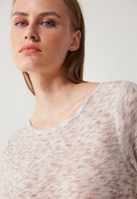 Heled värviga, tekstuuriga kootud topp, millel on ümmargune kaelus. Kangas näitab peent täpilist mustrit pehmes beežis ja kreemises toonis.