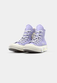 High-top sneakers in light purple canvas, featuring white laces, a rubber toe cap, and floral accents on the upper and sole.