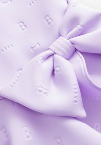 Lavanda tkanina s izrazitim mašnu in odtisnjenim besedilom. Gladka tekstura s subtilnimi vzorci mašnic in črk 'B' po vsej površini.