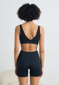 Black ribbed sports bralette with a deep V-back, paired with high-waisted shorts, featuring a smooth, stretchy texture and minimal design.