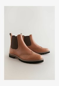 Botas Chelsea de cuero en color marrón claro con paneles laterales elásticos en marrón oscuro, detalles brogue en la puntera y suela de goma para tracción.