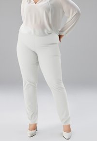 Pantalons blancs ajustés avec une texture lisse. Portés avec un haut léger blanc à encolure en V et détails à cordon.