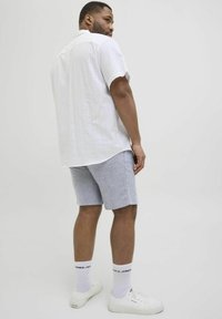 Chemise blanche à manches courtes avec un motif texturé, associée à un short bleu et des baskets blanches ; vue de dos.