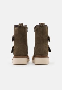 Bottines en daim marron avec double zip, deux boucles décoratives et une semelle en caoutchouc texturé. Présente une semelle extérieure crème contrastante.