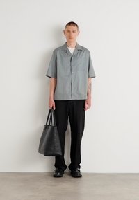 Camisa gris de manga corta con bolsillo, pantalones negros y una bolsa de mano negra; textura suave, diseño de botonadura y amplio cuello.