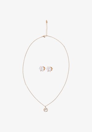 Finom arany lánc nyaklánc kis, kerek medállal, amelyet áttetsző kövek díszítenek, hozzáillő, kerek áttetsző kővel ékesített fülbevalókkal párosítva.