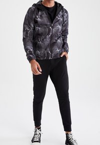 Sort og grå jakke med abstrakt mønster, lynlås foran, hætte, elastiske manchetter, parret med sorte sweatpants og høje sneakers.