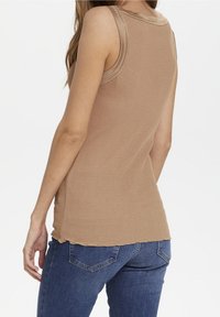 Brun ribbad linne med en figurnära passform, rå kant nederkant och vida ärmhål, tillsammans med blå jeans.