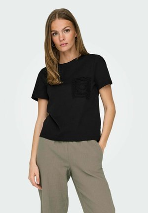 T-shirt nero in cotone con maniche corte, caratterizzato da una tasca quadrata testurizzata. Abbinato a pantaloni larghi in grigio-verde chiaro e testurizzati.