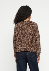 Tričko s leopardím potlačou, dlhý rukáv, v hnedých a čiernych odtieňoch. Mäkkaná látka, voľný strih a okrúhly výstrih. Skombinované s tmavomodrými džínsami.