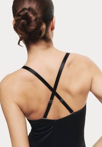 Bodysuit negro ajustado con tirantes cruzados y ajustables, y una textura suave. Espalda expuesta y sin adornos visibles.
