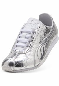 Ασημί μεταλλικό παπούτσι Puma με λευκά κορδόνια και υφή στην σόλα, που δείχνει πλευρικές και μπροστινές λεπτομέρειες σε λευκό φόντο.