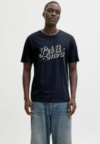 Must värviline puuvillane t-särk, millel on valge skripti tekst "Las see lumi sadada" koos lumehelbe aktsentidega, ühendatud helesiniste teksadega.