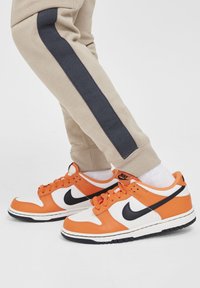 Nike Dunk Low sneakers hebben een leren bovenwerk in oranje en wit met zwarte accenten. De zool is wit met zwarte details, ontworpen voor casual gebruik.