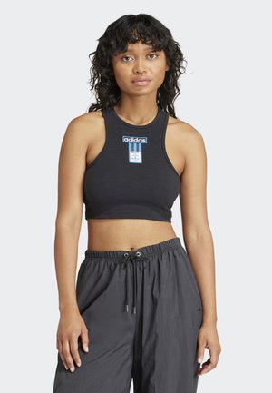 Svart ribbestrikket kort topp med en blå Adidas-etikett på brystet, i kombinasjon med løstsittende grå bukser. Enkelt design, uten ermer.