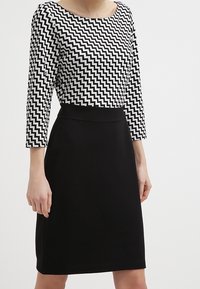 Robe noire avec une silhouette ajustée et une jupe au genou, associée à un haut à motif zigzag noir et blanc avec un col bateau et des manches trois-quarts.