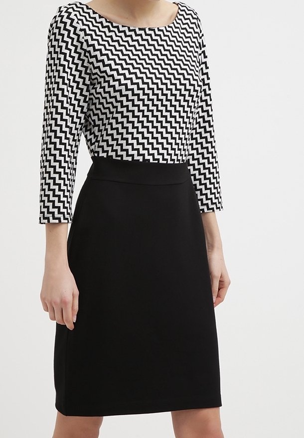 Robe noire avec une silhouette ajustée et une jupe au genou, associée à un haut à motif zigzag noir et blanc avec un col bateau et des manches trois-quarts.