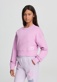 Felpa cropped rosa con maniche lunghe, scollatura rotonda, polsini a costine e un'etichetta tessuta. Tessuto morbido con un design casual.