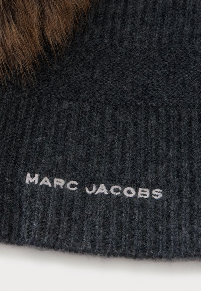 Gros plan sur un tissu tricoté gris foncé avec "MARC JACOBS" brodé en fil blanc et détail de fourrure marron sur le bord supérieur.