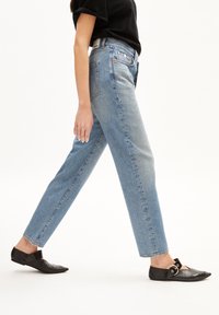 Vaqueros rectos de color azul claro, hechos de mezclilla, con una cintura de altura media y un diseño clásico de cinco bolsillos, combinados con zapatos planos negros.