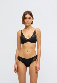 Melns mežģīņu krūšturis ar smalku ziedu rakstu un stīpiņu, komplektā ar atbilstošām bikini biksītēm ar mežģīņu sānu akcentiem.