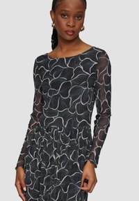 Schwarzes langärmeliges Kleid mit weißem Blumenmuster, tailliertem Oberteil und gerafftem Bund. Durchsichtige Ärmel mit strukturierten Details.