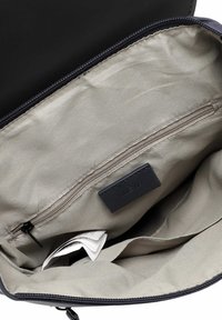 Intérieur d'un sac noir avec une doublure beige, comprenant une poche zippée et une étiquette. Tissu lisse avec un léger éclat ; détails de couture minimaux.
