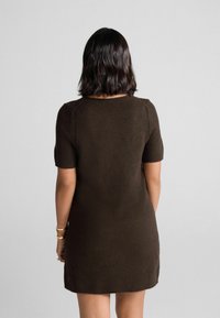 Braunes Strickkleid mit kurzen Ärmeln, rundem Ausschnitt, figurbetontem Schnitt und geripptem Saum. weiche Textur mit minimalen Details.
