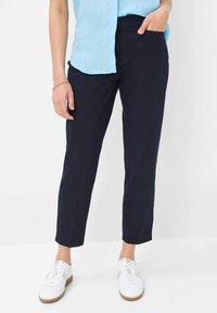 Navy tapered broek met een gladde textuur, voorzien van zijzakken en een mid-rise taille. Gecombineerd met witte sneakers voor een casual look.