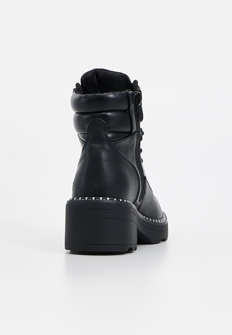 Botines de cuero negro con un cuello acolchado, cremallera lateral y un tacón grueso en bloque. Presenta costuras contrastantes a lo largo de la suela.
