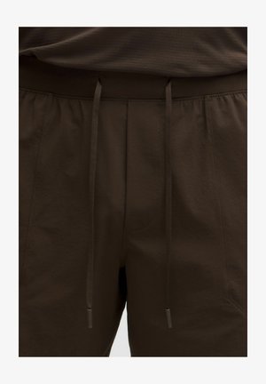 Primer plano de pantalones de color marrón oscuro con una cinturilla elástica y cordones ajustables en el centro delantero.