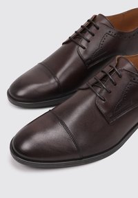 Zapatos de vestir de cuero marrón con un acabado pulido, que cuentan con punta cap, perforaciones decorativas y cierre de cordones.