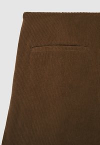 Gamba di pantaloni in tessuto rigato marrone con una tasca a welt orizzontale vicino al bordo superiore, su uno sfondo chiaro e semplice.