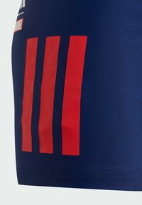Námořnické sportovní šortky s třemi vertikálními červenými pruhy a hladkou texturou. Obsahují elastický pas a švové detaily lemování.