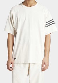 Loose-fit cream cotton t-shirt featuring a round neckline, short sleeves, and three dark gray stripes on the left sleeve with a small black logo.