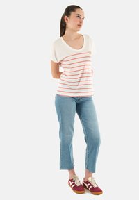 Camiseta blanca a rayas con líneas coral y detalle de bolsillo, combinada con jeans cortos de color azul claro y zapatillas rojas con acentos blancos.