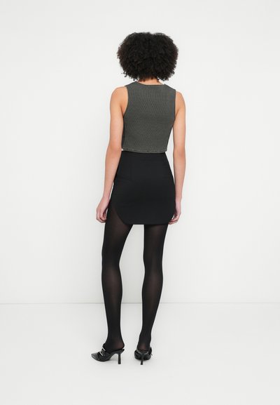 Top court côtelé gris associé à une mini-jupe noire et des collants noirs transparents. Le mannequin porte des chaussures à talons hauts noires.