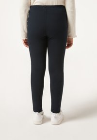 Marineblaue Leggings aus einem glatten, elastischen Stoff mit anliegendem Schnitt, knöchellang, getragen mit weißen Turnschuhen.