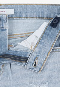 Šviesiai mėlynos spalvos džinsai su platėjančiu dizainu. Turi užtrauktuko skrydį, sagos užsegimą ir šiurkščiai apdorotas kraštines. Auksinė siūlė kontrastuoja su audiniu.