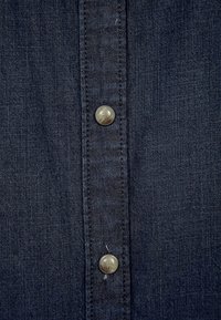 Mörk denimskjorta med knäppning fram, två metallknappar och subtil textur, som visar en klassisk blå färg.