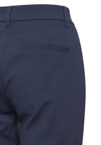 Pantalon tailleur bleu marine vu de dos, avec poche passepoilée et passants de ceinture sur fond blanc.