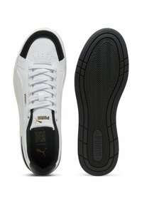 Adidași albi cu vârf negru, talpă texturată neagră, șireturi plate și branding auriu pe lateral și pe limbă. Partea superioară din piele fină.