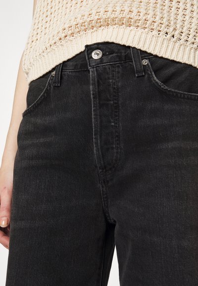 Black denim jeans featuring a high waist, front pockets, and silver button hardware. The texture is smooth with a slight sheen.