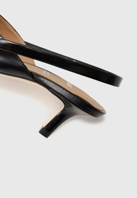 Zwarte gepatineerde leren sandalen met hak, voorzien van slanke banden, een puntige neus en een lage blokhak. Het interieur heeft een beige inlegzool.